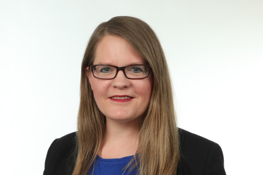 Lächelnde Frau mit Brille vor einem weißen Hintergrund. 