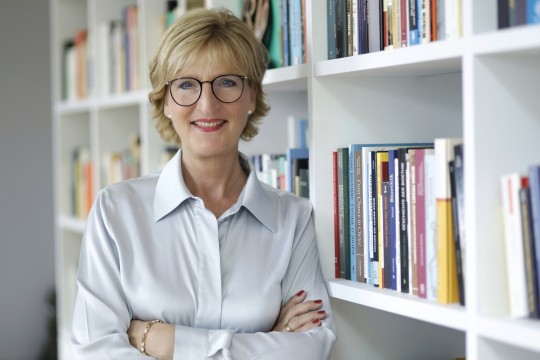 Lächelnde Frau, die vor einem Bücherregal steht. 