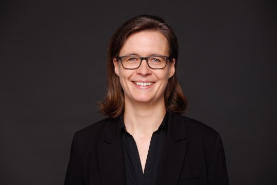 Frau mit Brille vor dunklem Hintergrund. 