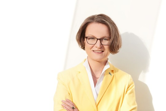 Frau mit einem gelben Blazer vor einem hellen Hintergrund.
