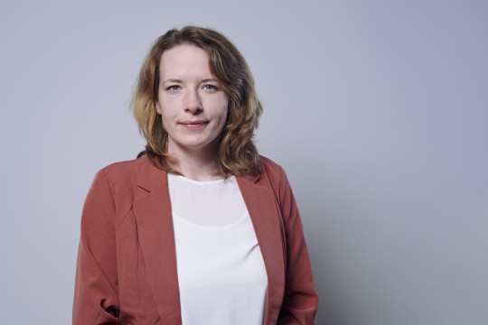 Lächelnde Frau vor einem grauen Hintergrund. 