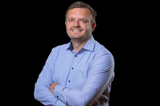 Lächelnder Mann vor einem dunklen Hintergrund. 