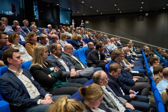 Großer Saal mit sitzendem Publikum. 