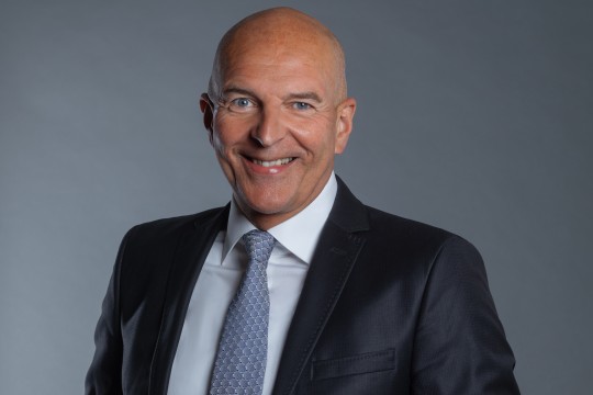 Lächelnder Mann vor einem grauen Hintergrund. 